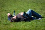 A drunk person passed out next to a bottle of alcohol on grass.