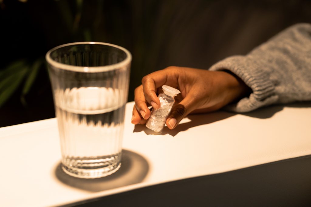 A glass containing a drink right next to a hand holding a bottle of pills.