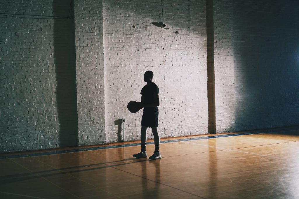 Man standing in a basketball court with a basketball in hand.
