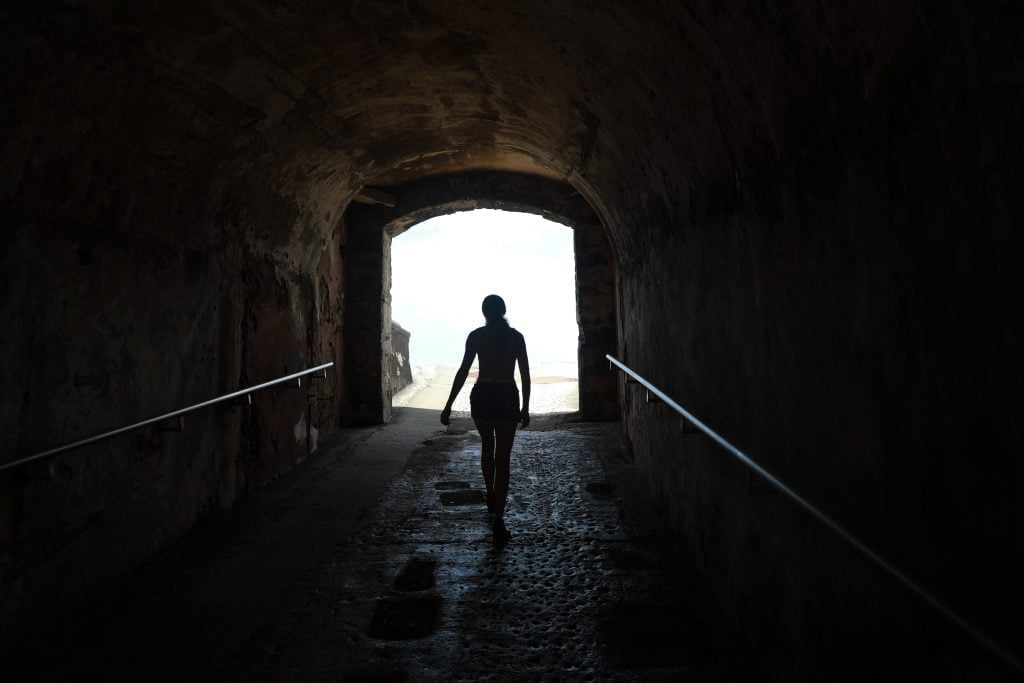 Woman walking out of a dark tunnel with light at the end.