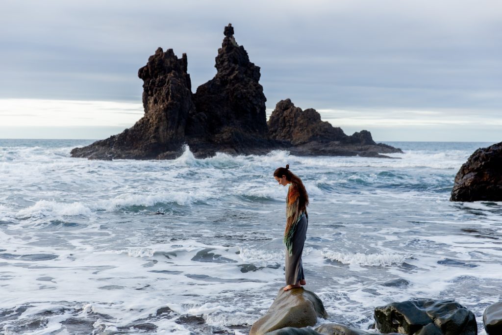 A person standing on a rock in front of the sea alone.