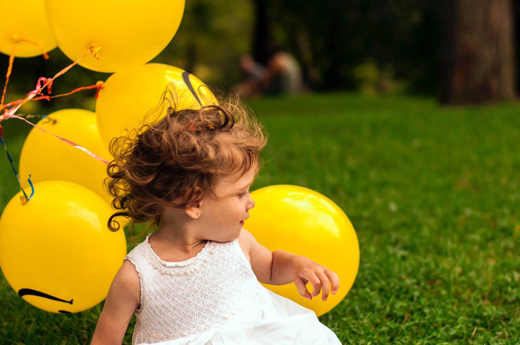 A child sitting on grass with yellow balloons behind.