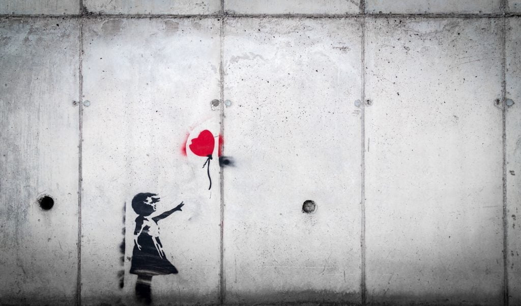A painting on the wall in black of a child reaching for a red balloon.