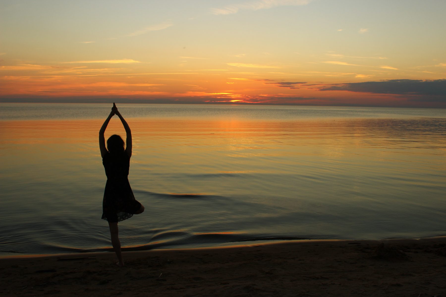 A person doing yoga facing the sea at sunset.