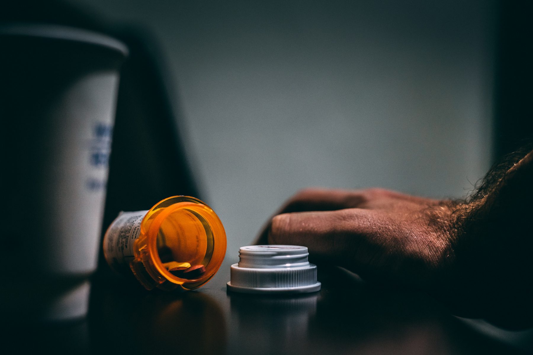 A spilled pill bottle next to a cup and a hand.