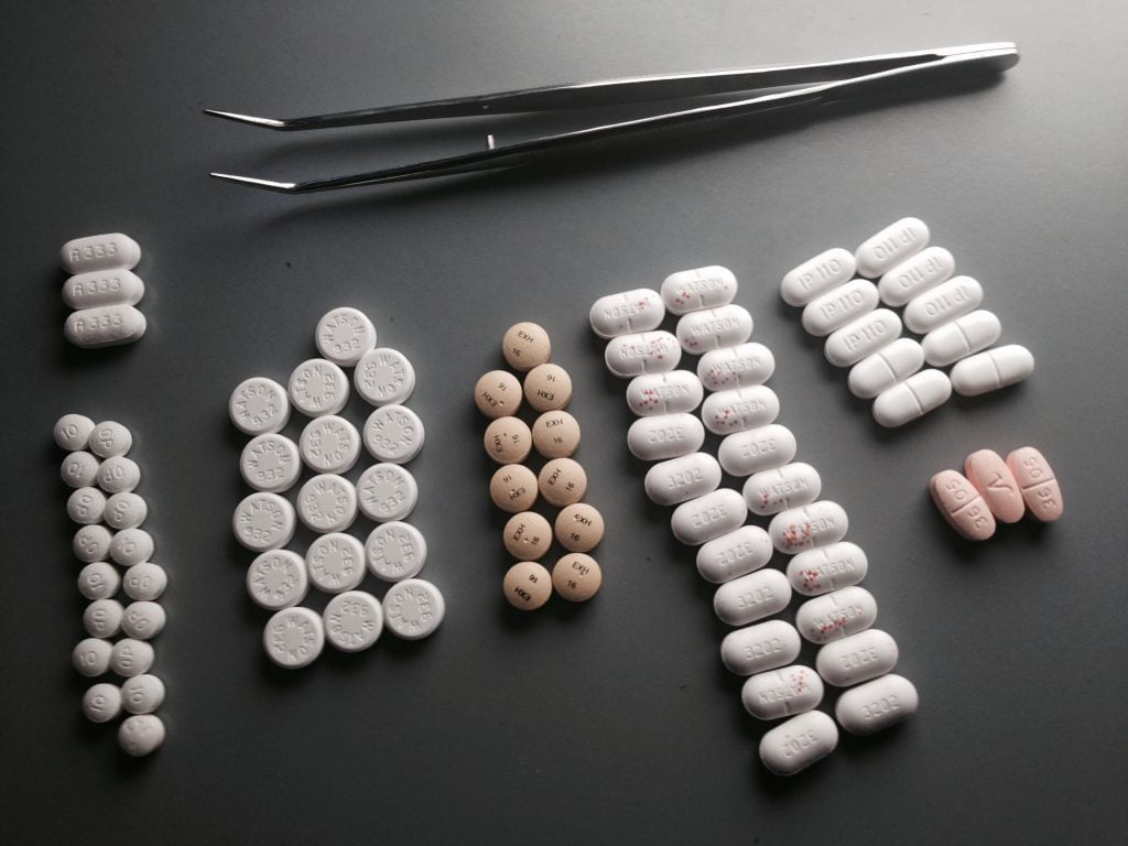 Seven sets of pills arranged on a table with tweezers.