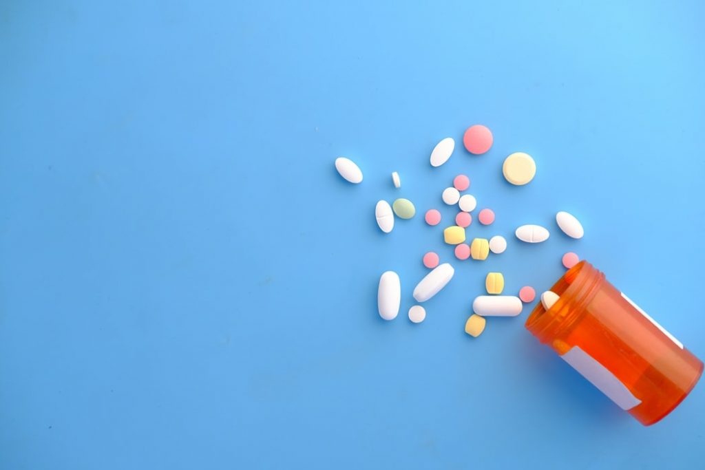 A spilled orange pill bottle with colorful pills spilling out.