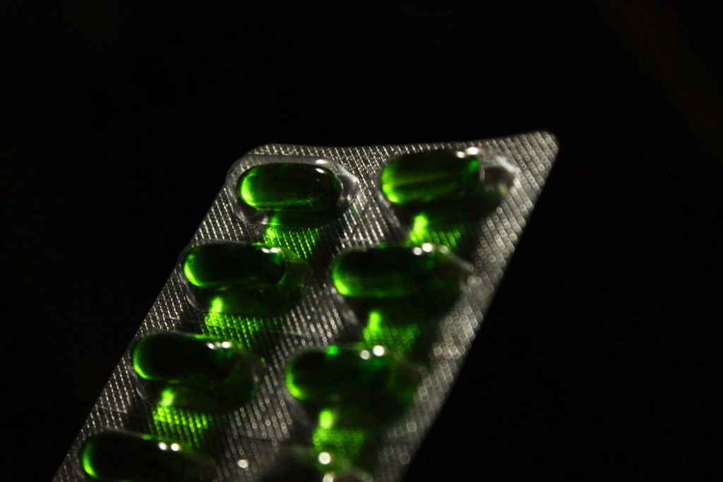 A sachet of green pills with a black background.