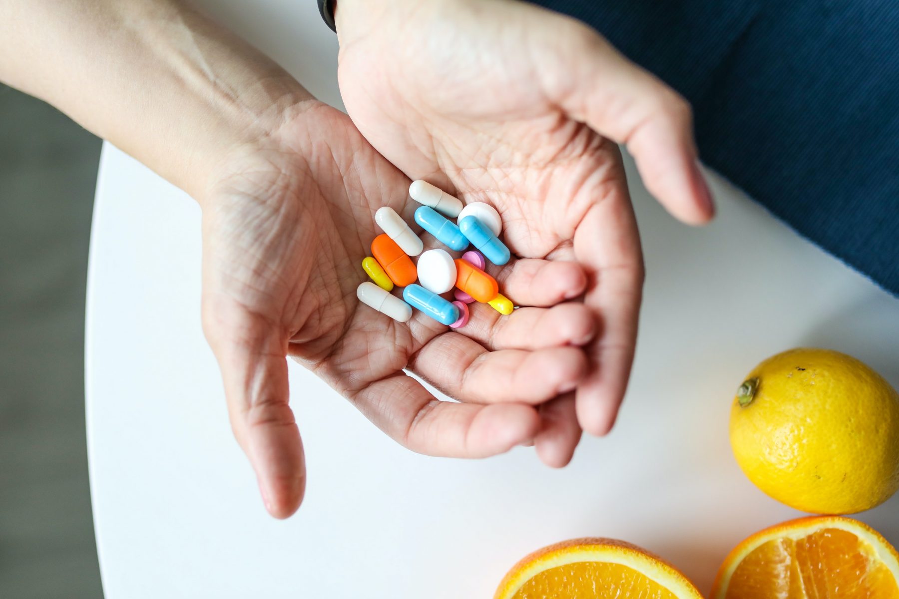 A bunch of colorful pills in the palms of a person's hands, next to some lemons.