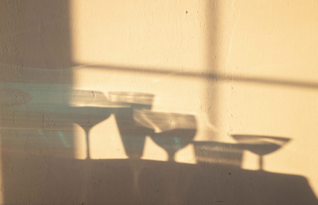 Shadows on a white wall of glasses with alcoholic beverages.